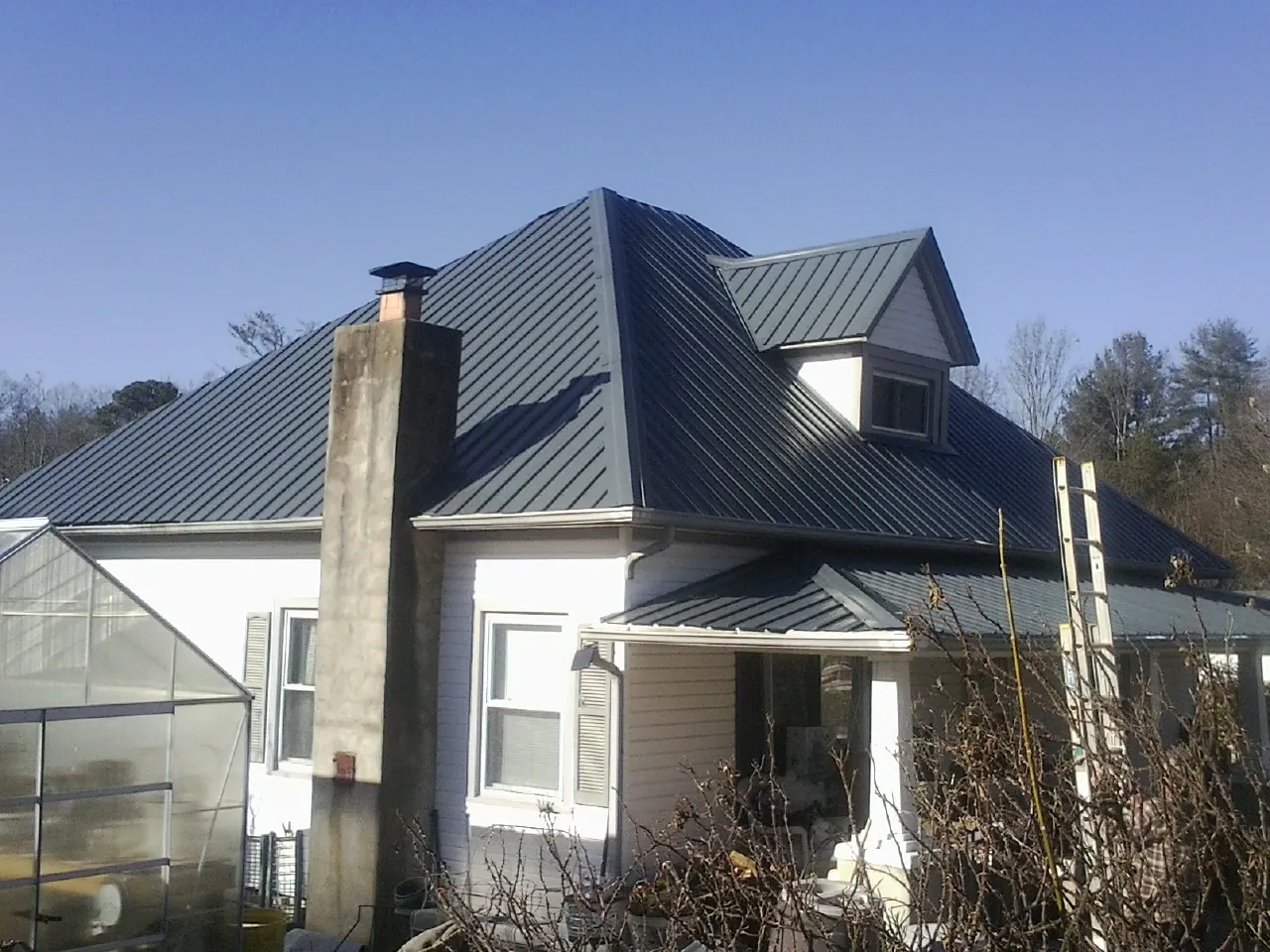 Dark blue standing seam metal roof on a white farmhouse with dormer — Slate & Tile Roof Repair by Roofing Brothers in Dushore