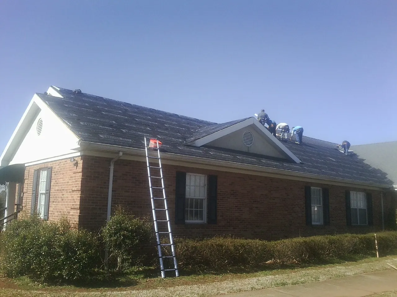 Crew tearing shingles off a brick ranch roof with a ladder set — Emergency Roof Repair work by our crew in Dushore