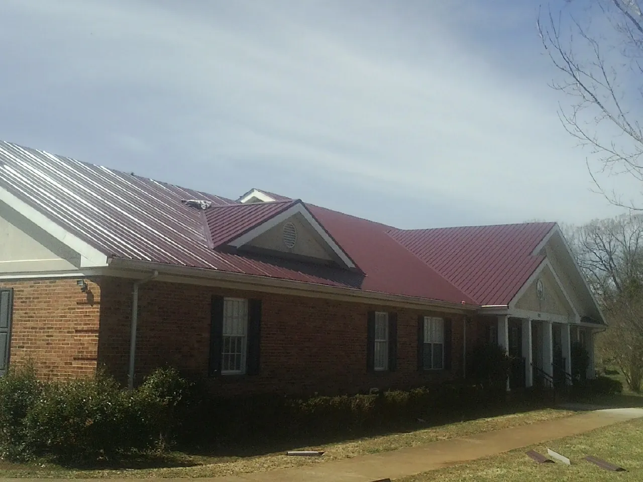 Red metal roof with gabled entries on a long brick building, from a Hail Damage Roof Repair job in Dushore