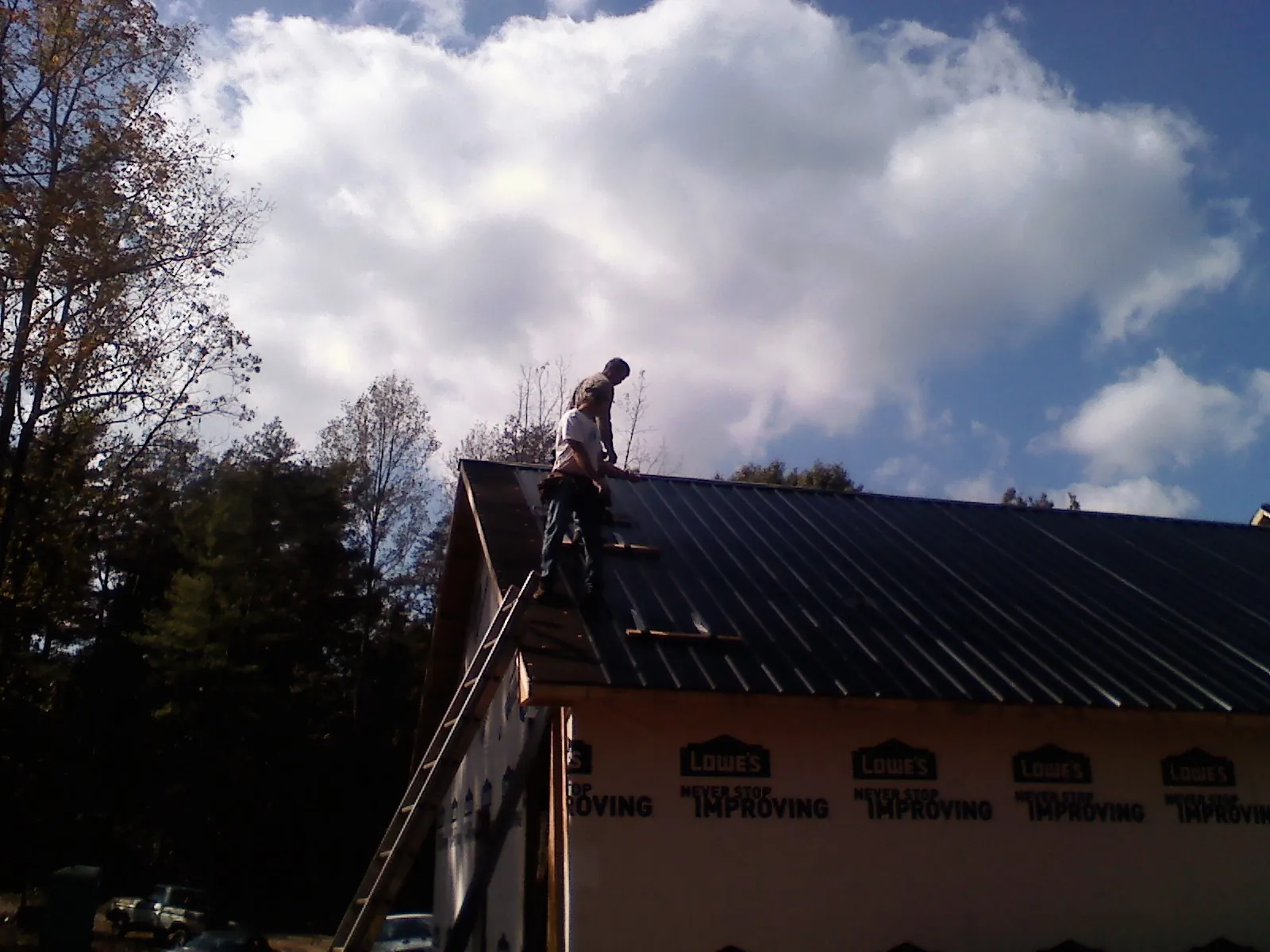Roofer fastening dark metal panels high against a cloudy sky, from a Roof Inspection job in Dushore