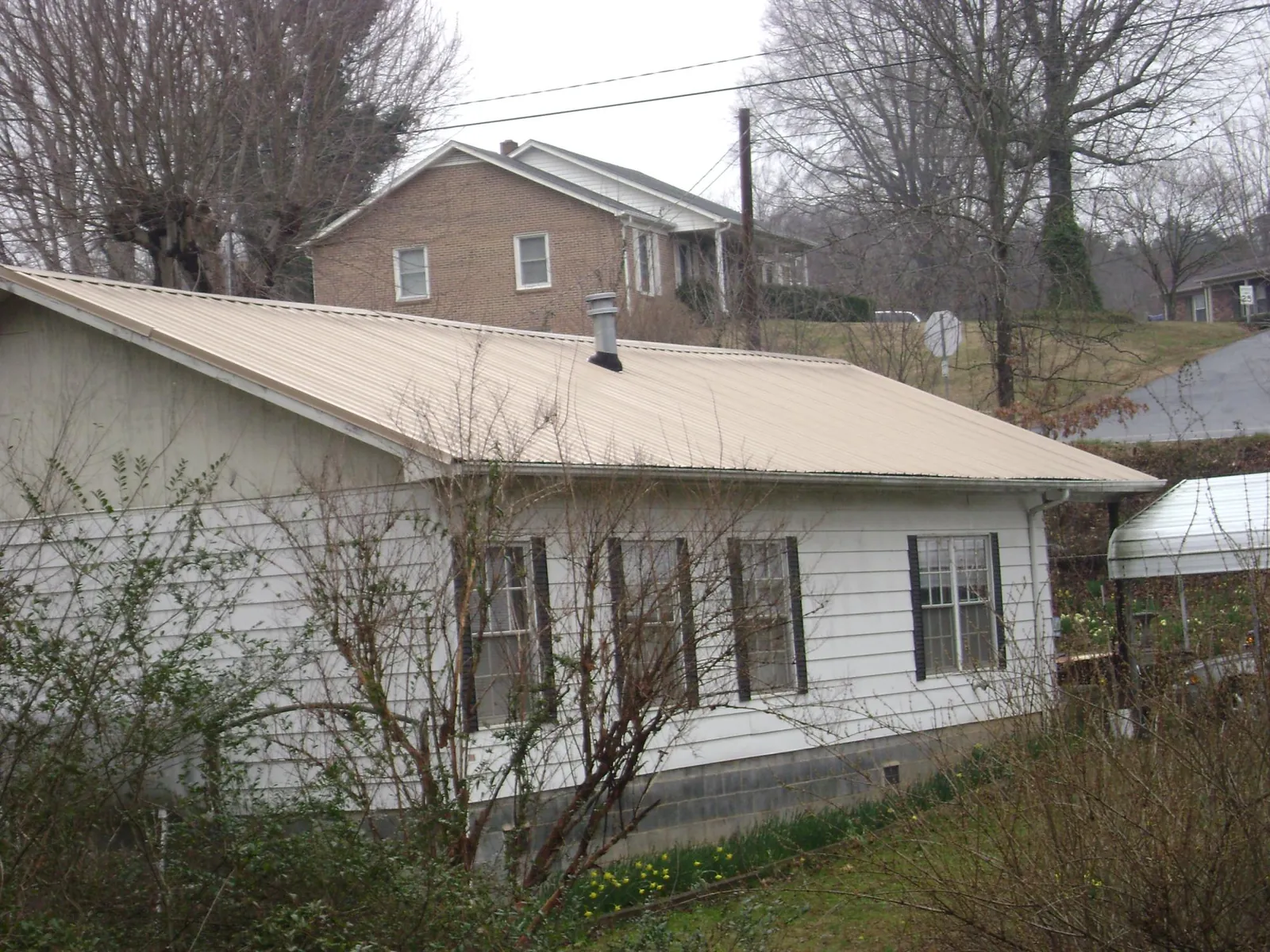 Tan metal roof on a white sided house set into a hillside — Commercial Roofing by Roofing Brothers in Dushore
